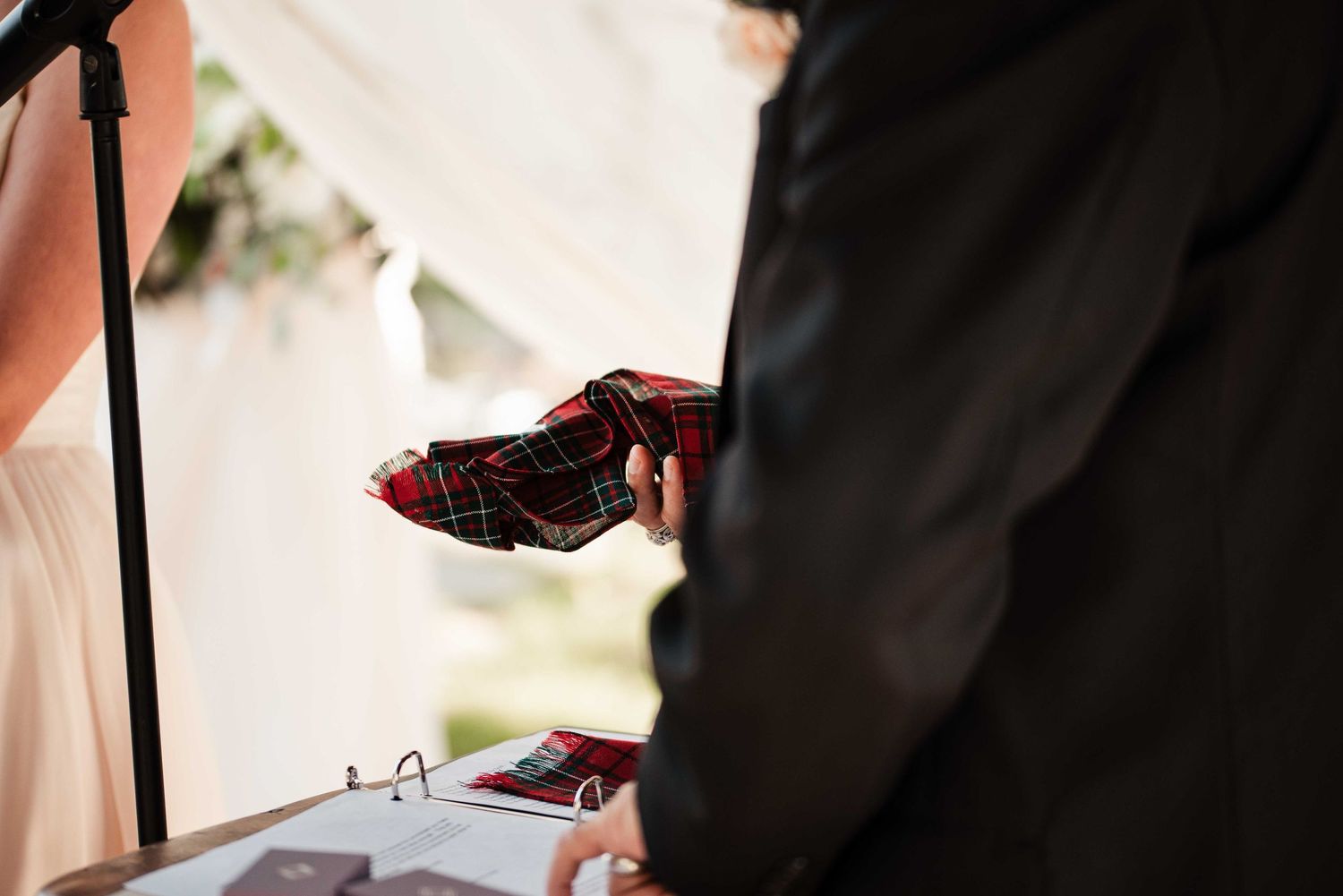 Person holding a red tartan plaid fabric pouch during an outdoor wedding ceremony.