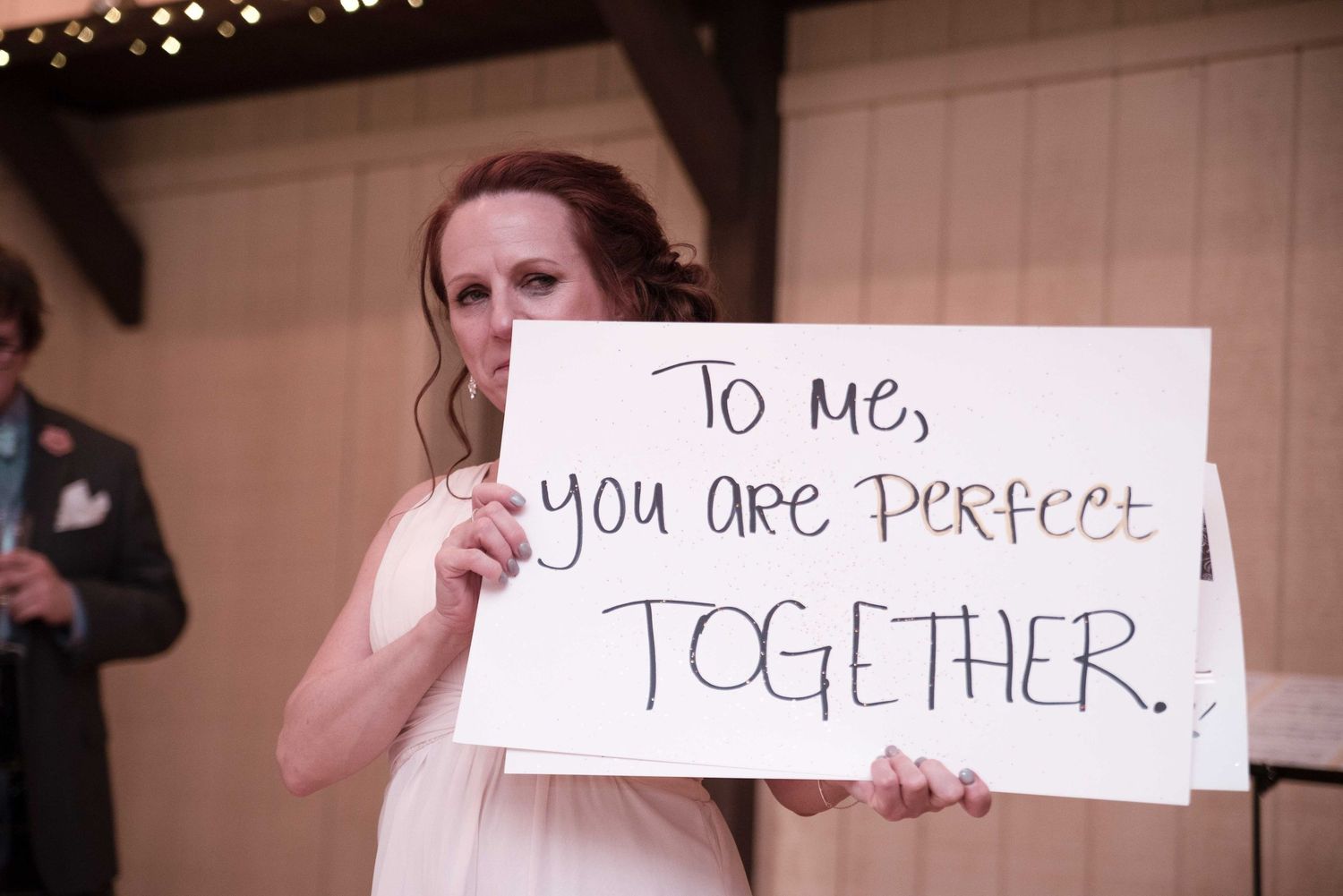 Bride holds a sign reading 'To me, you are perfect together' at a wedding reception.