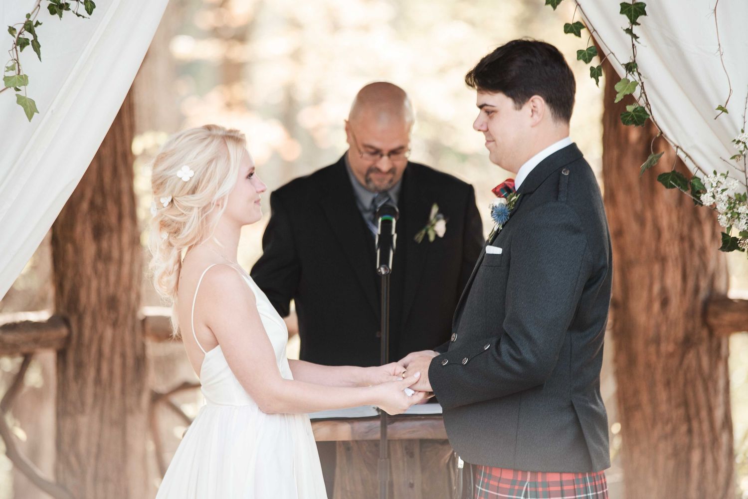 Bride and groom holding hands during outdoor wedding ceremony with officiant.
