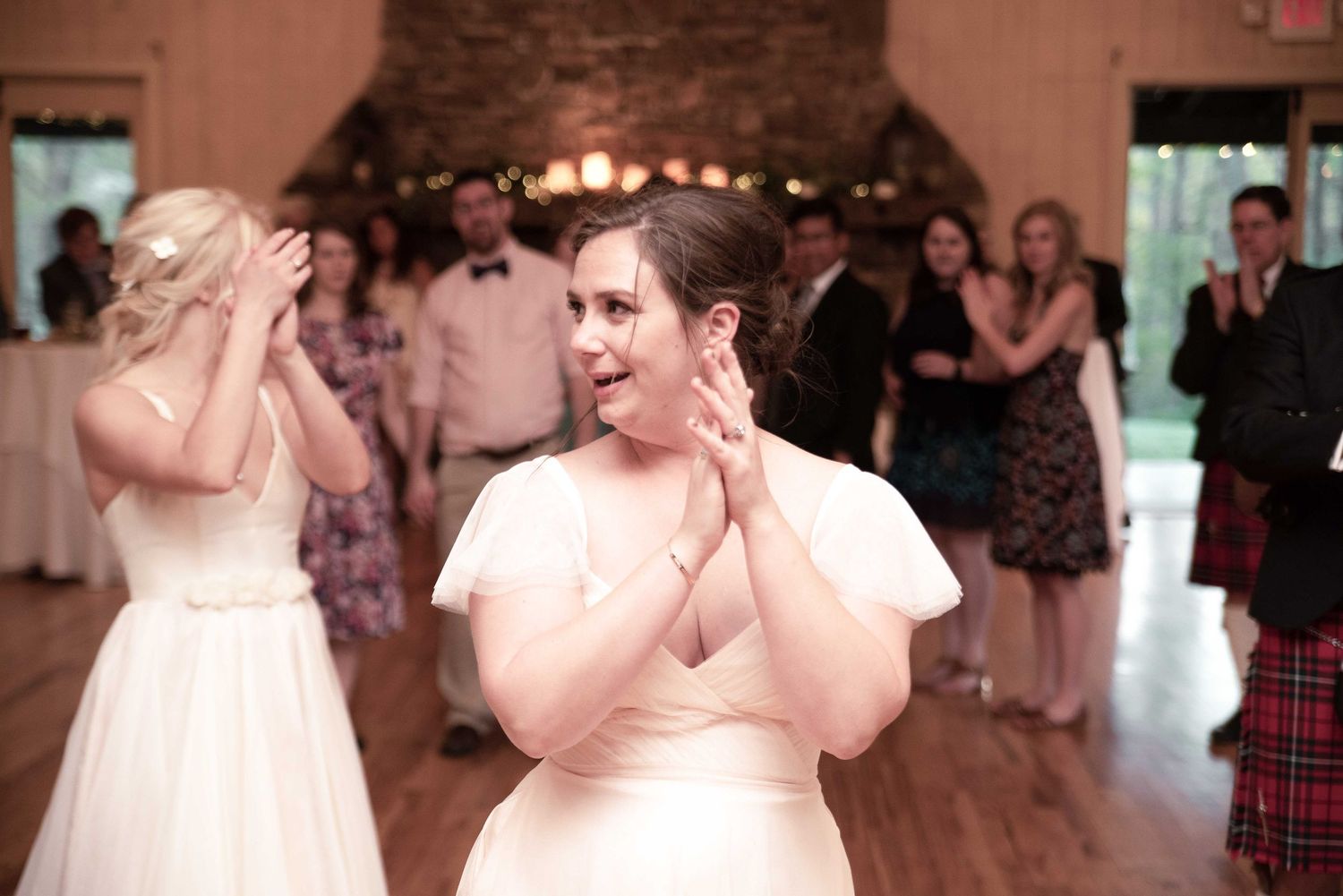A woman in a white wedding dress claps and smiles on the dance floor at a wedding reception.