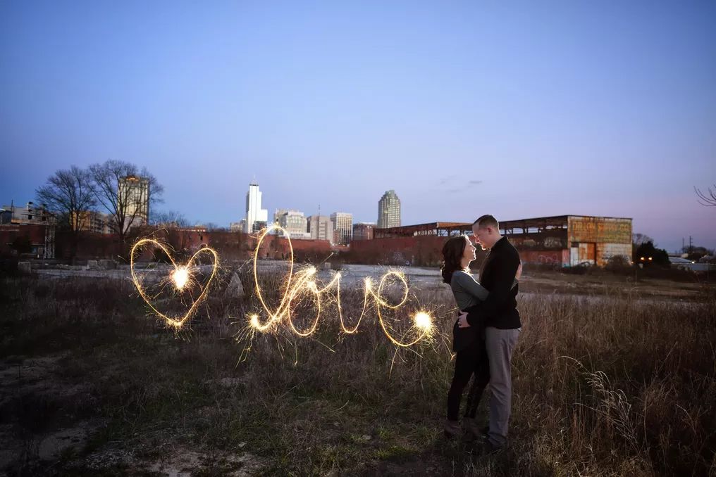 Couple kissing at dusk with sparkler light painting spelling love and heart shapes.