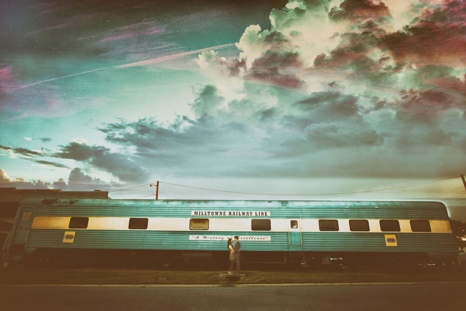 Lone figure stands before vintage passenger train under dramatic cloudy sky at dusk.