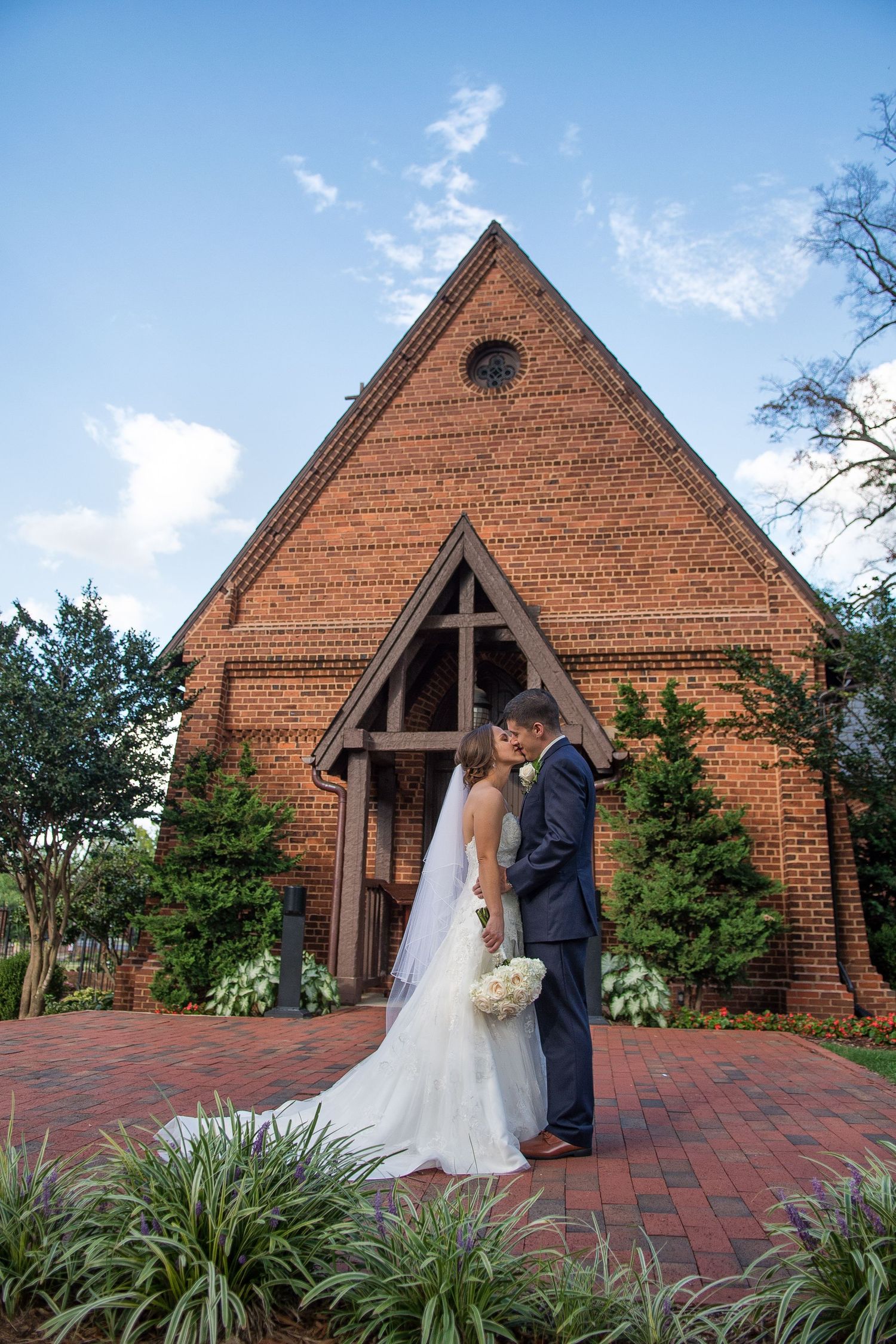 Newlyweds share a romantic kiss outside a charming brick chapel on their wedding day.