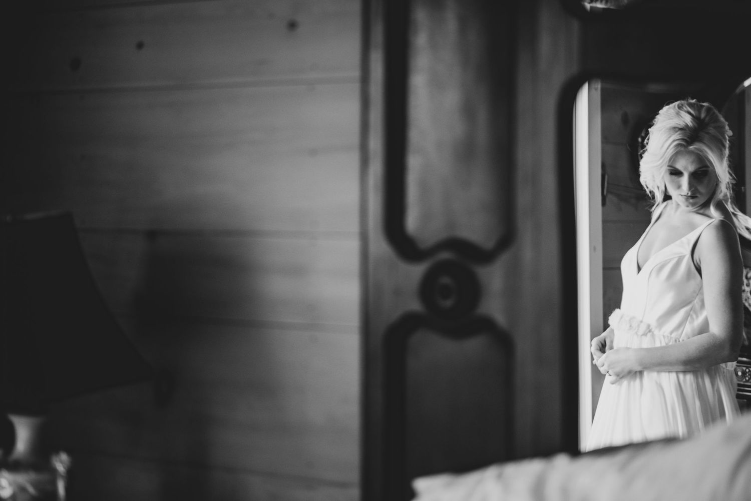 A black and white photo of a bride in a wedding gown gazing into an ornate mirror.