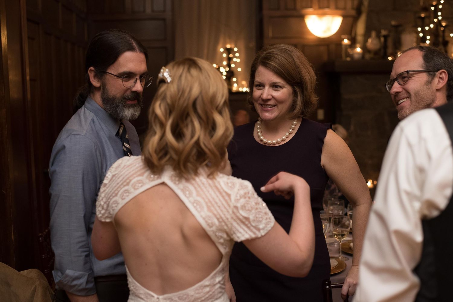 Guests socializing at an elegant wedding reception in a dimly lit venue, bride in backless lace gown.
