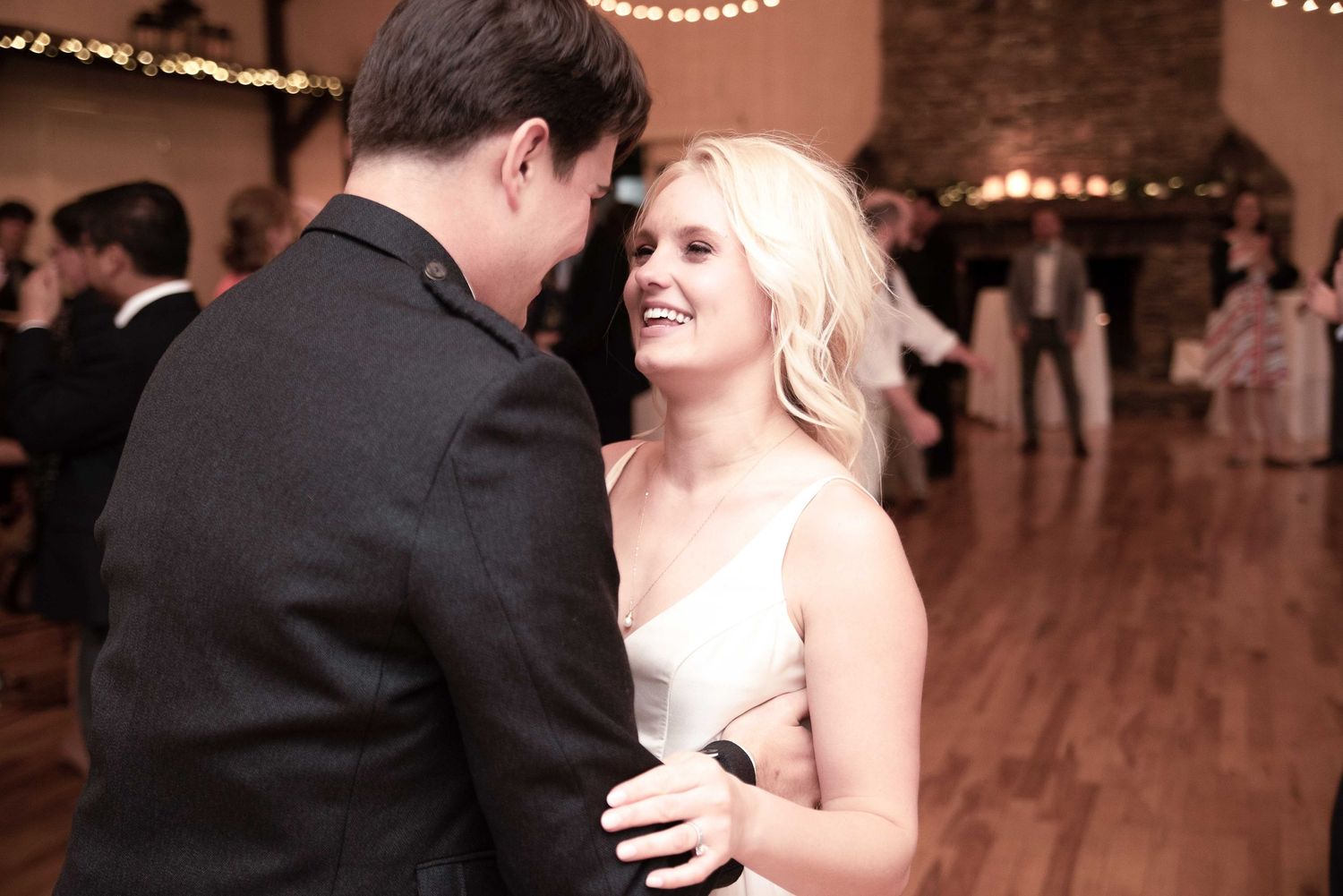 Couple sharing a romantic first dance at a wedding reception in a warmly lit rustic venue.