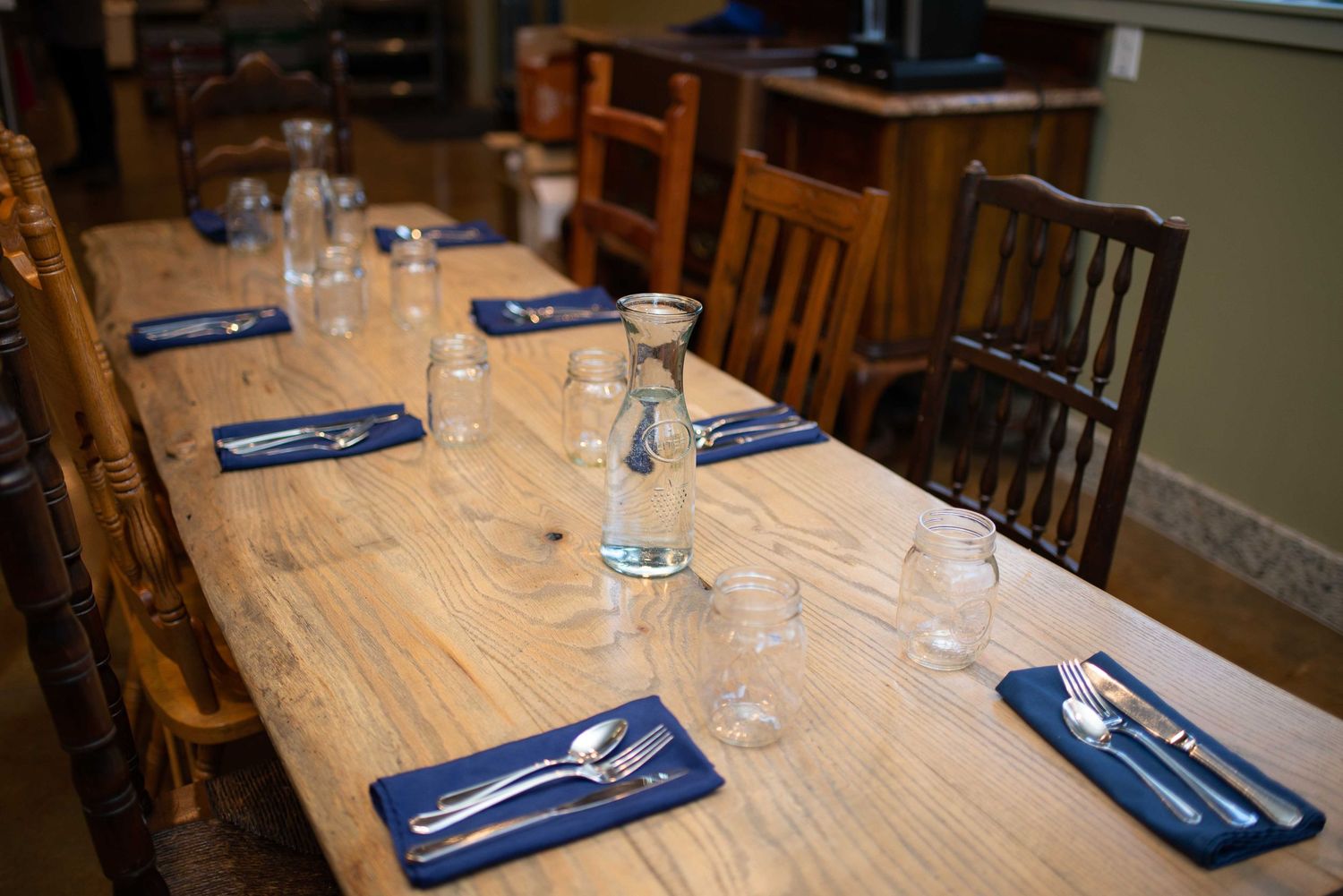 Rustic wooden dining table set with blue napkins, silverware, and glass carafes in a cozy restaurant setting.