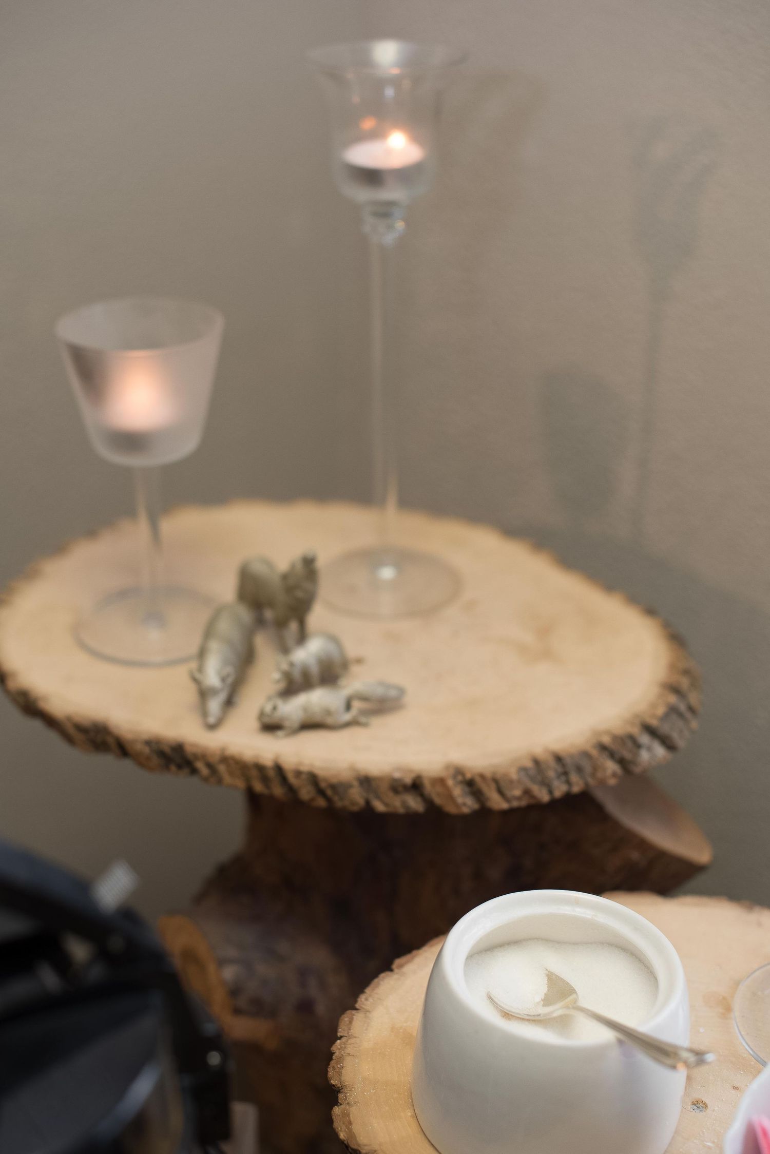 Rustic wood slice display with candles, decorative figurines, and a white bowl with spoon on tiered tree stump stands.