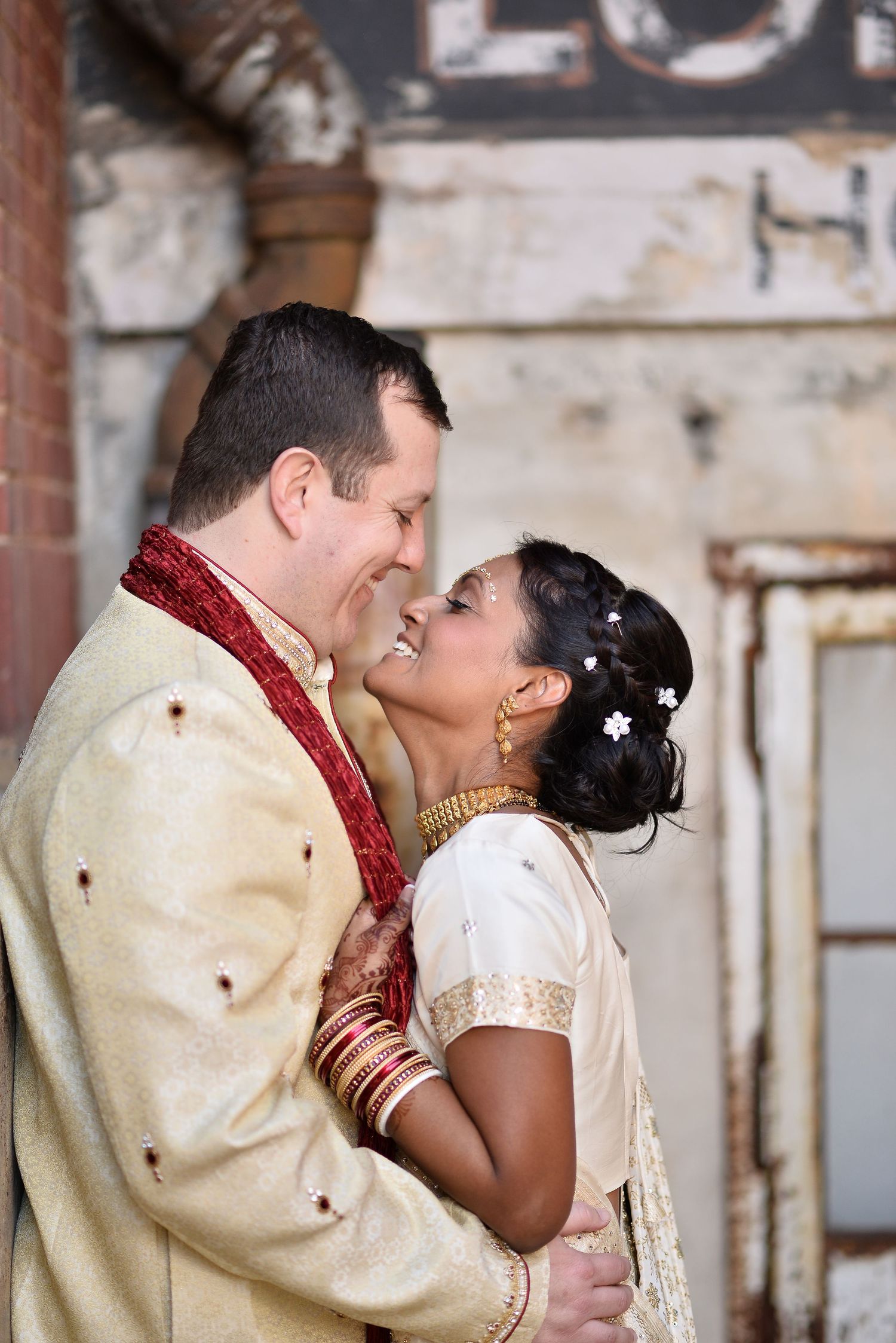 Couple in traditional Indian wedding attire share a romantic moment, smiling and embracing outdoors.