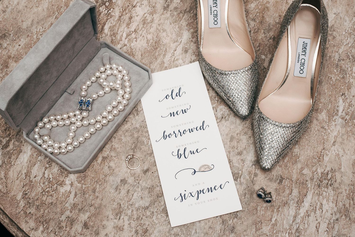 Elegant wedding flat lay with Jimmy Choo glitter heels, pearl necklace, and old new borrowed blue sixpence card.