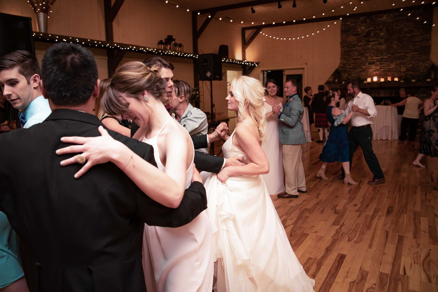 Bride and groom share first dance at elegant indoor wedding reception with string lights and stone walls.