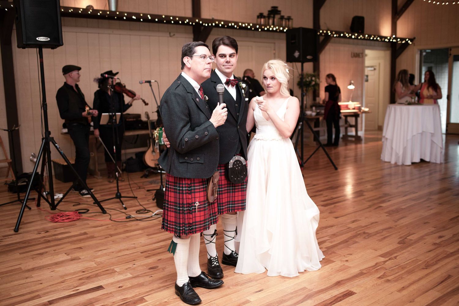 Bride and groom share a microphone during wedding reception toast, with live band and wood dance floor.