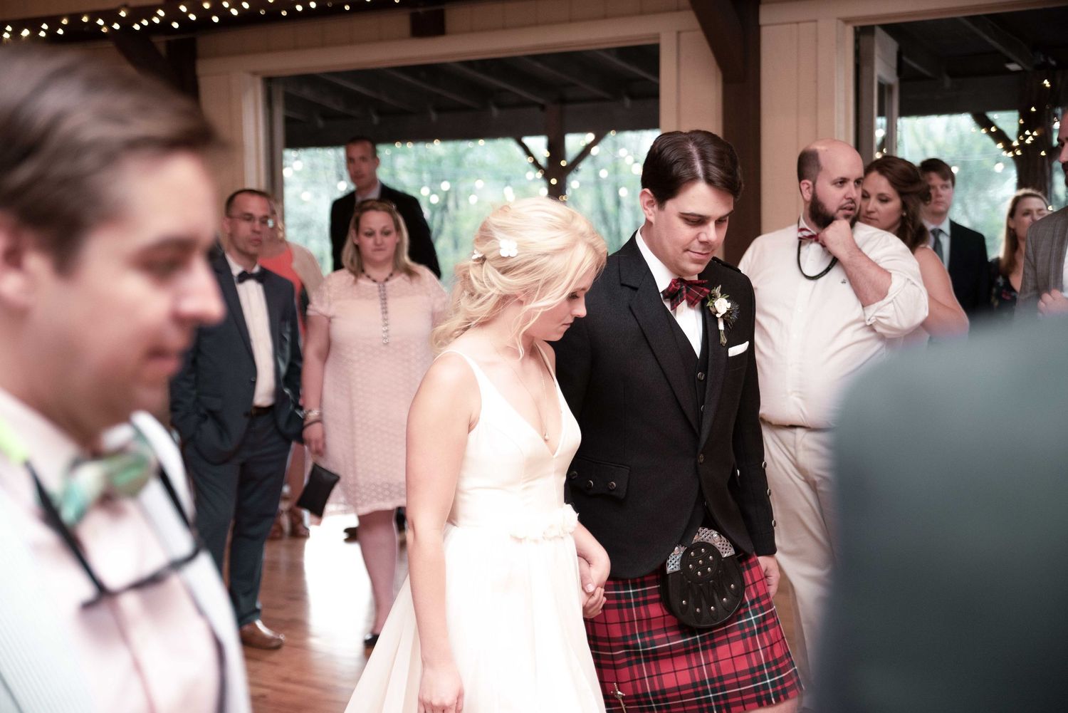 Bride and groom in Scottish kilt walking together at elegant indoor wedding reception celebration.