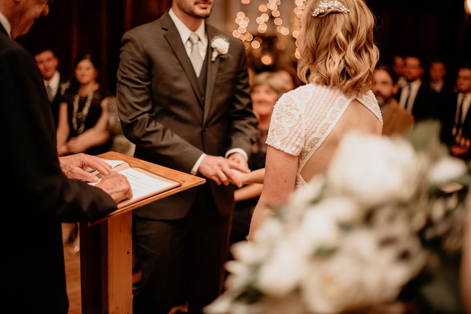 Bride and groom exchanging vows at wedding altar, holding hands with officiant and floral arrangements nearby.