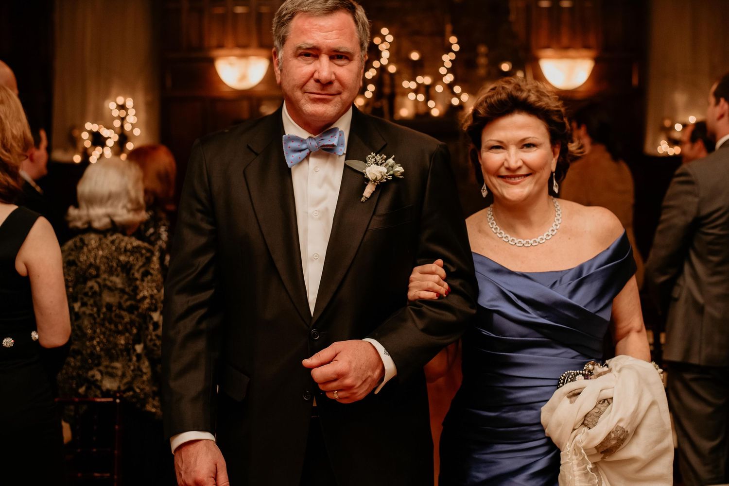 Elegant couple posing at a formal wedding reception, man in tuxedo with bow tie, woman in blue off-shoulder gown.