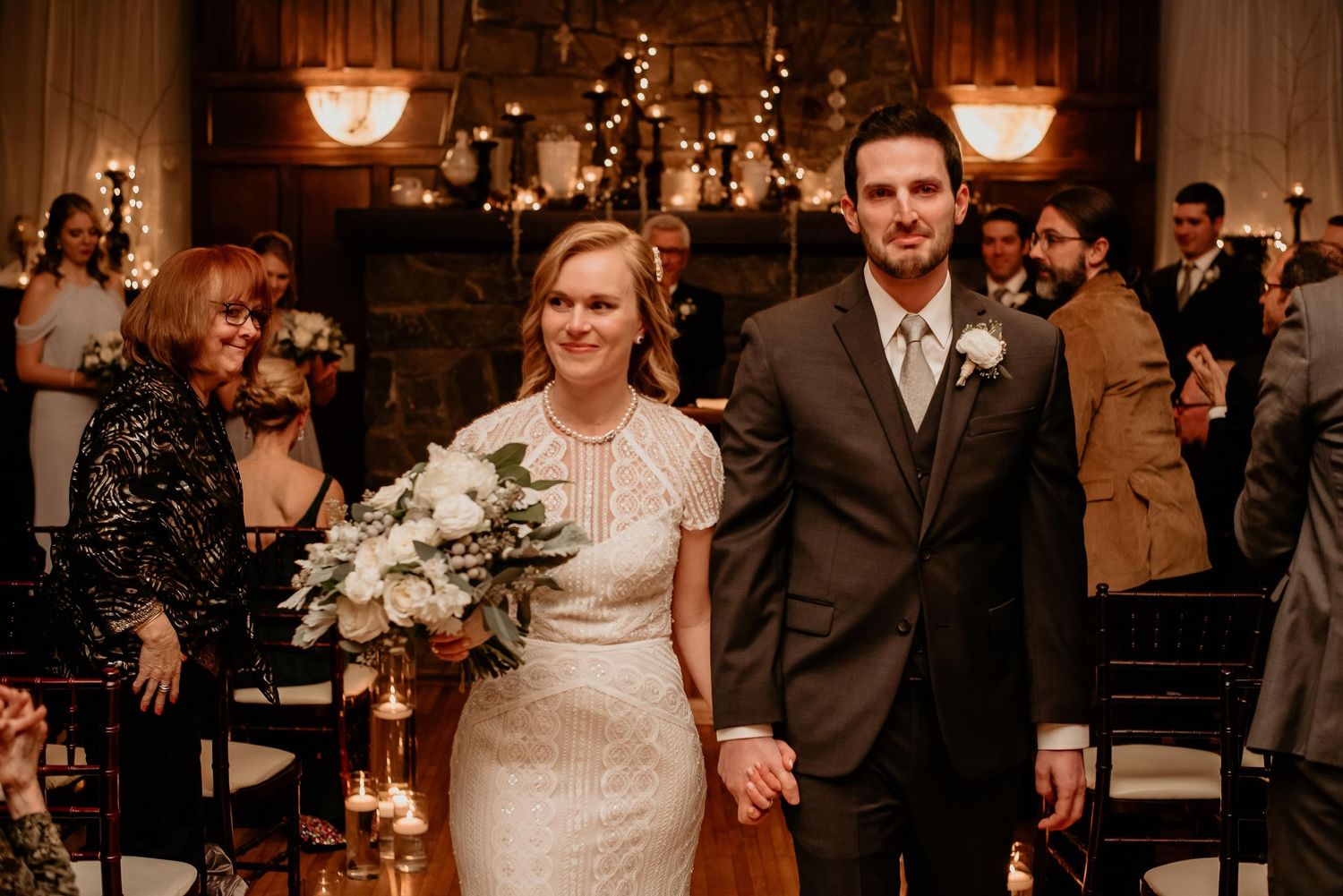 Bride and groom walk down the aisle hand in hand after wedding ceremony in warmly lit rustic venue.