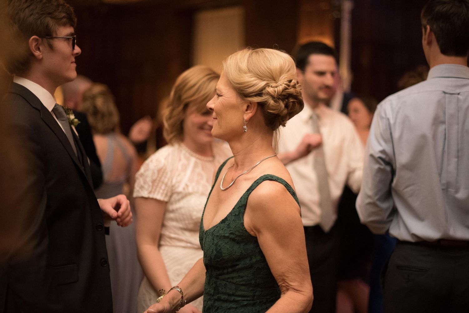 Guests mingling at an elegant wedding reception, woman in green dress socializing in warmly lit venue.