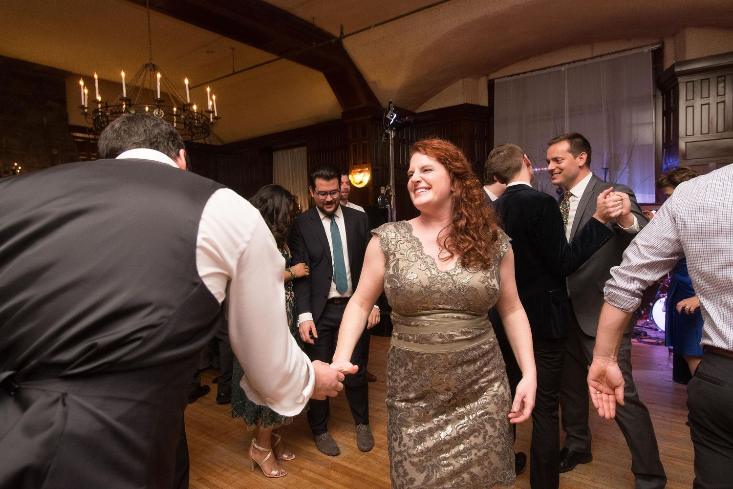 Guests dancing joyfully at an elegant wedding reception in a warmly lit venue with chandeliers.