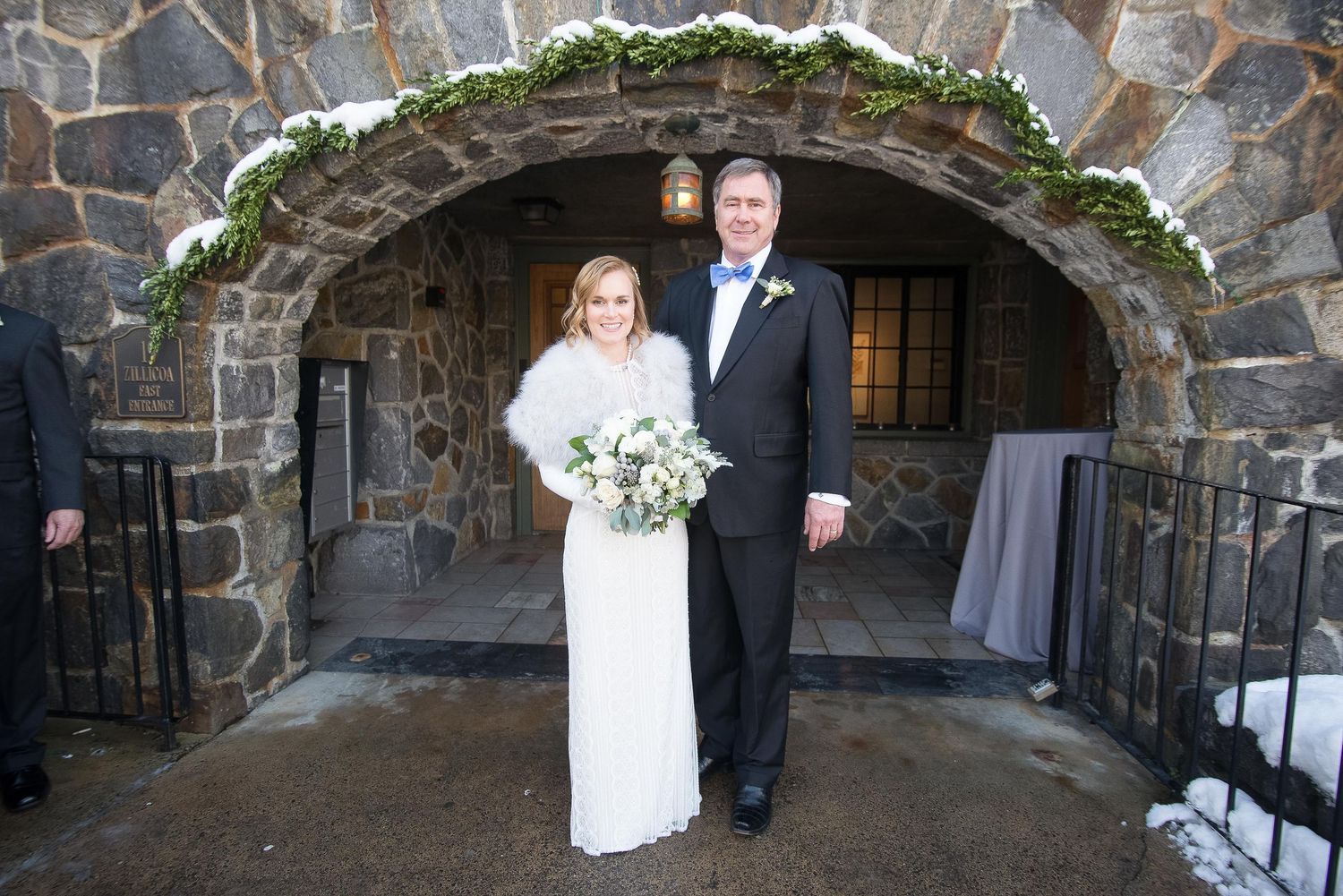 Bride and groom posing under a stone arch adorned with greenery at a winter wedding venue.