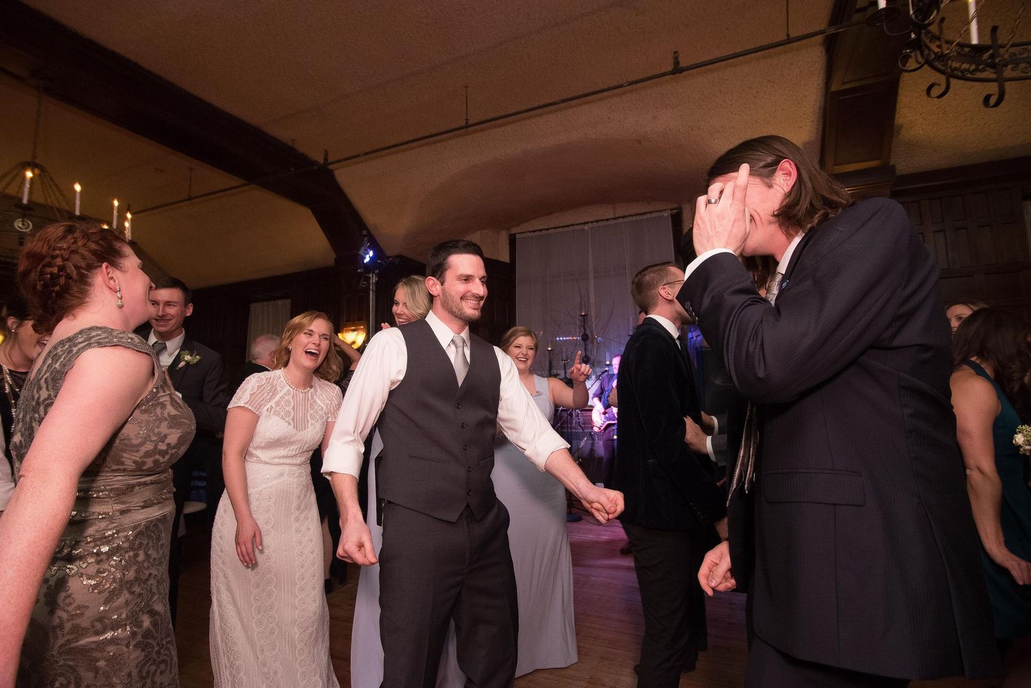 Joyful wedding reception guests dancing and laughing together in an elegantly lit venue with candlelight ambiance.