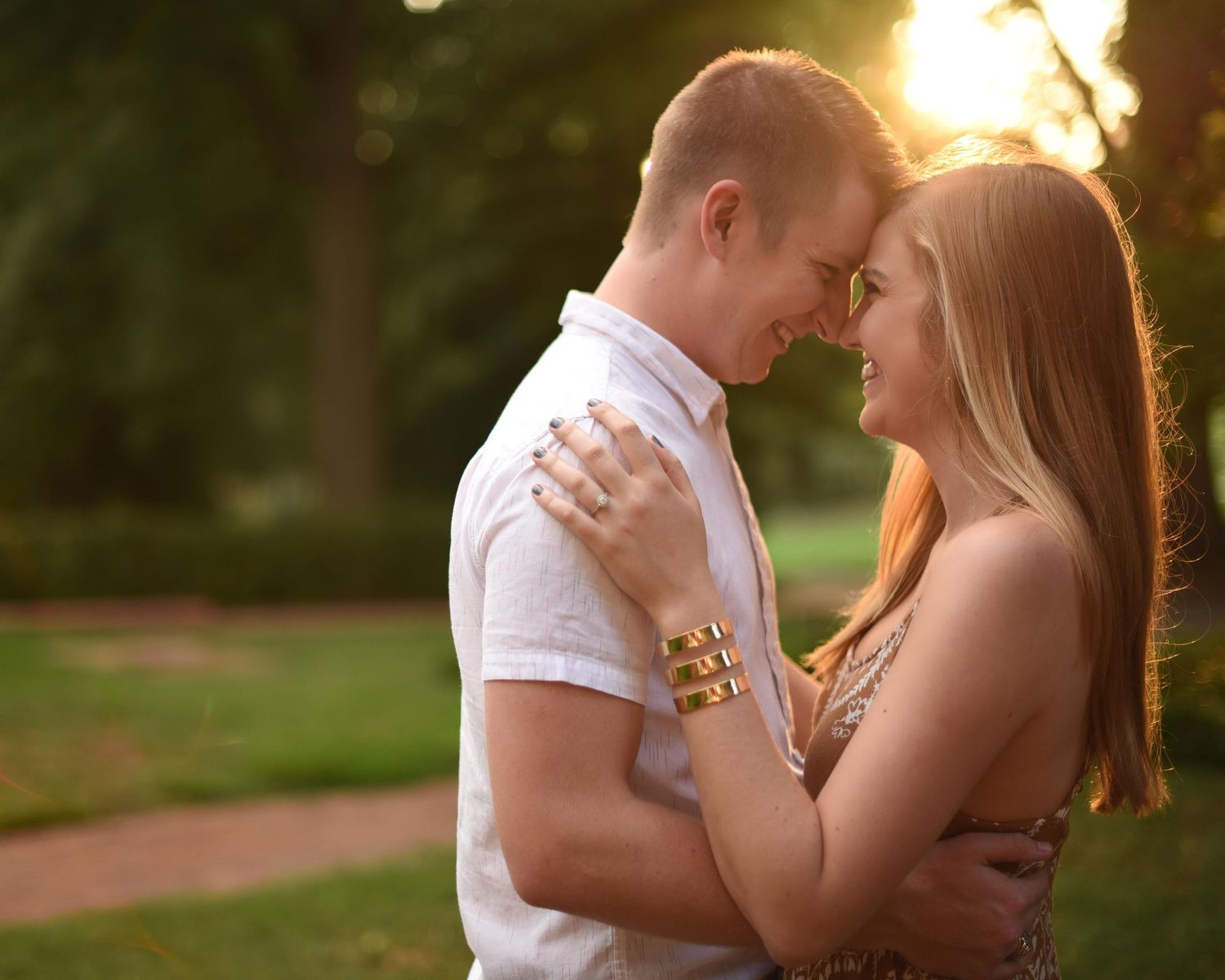 A loving couple embraces outdoors during a warm sunset, smiling closely together in a park.