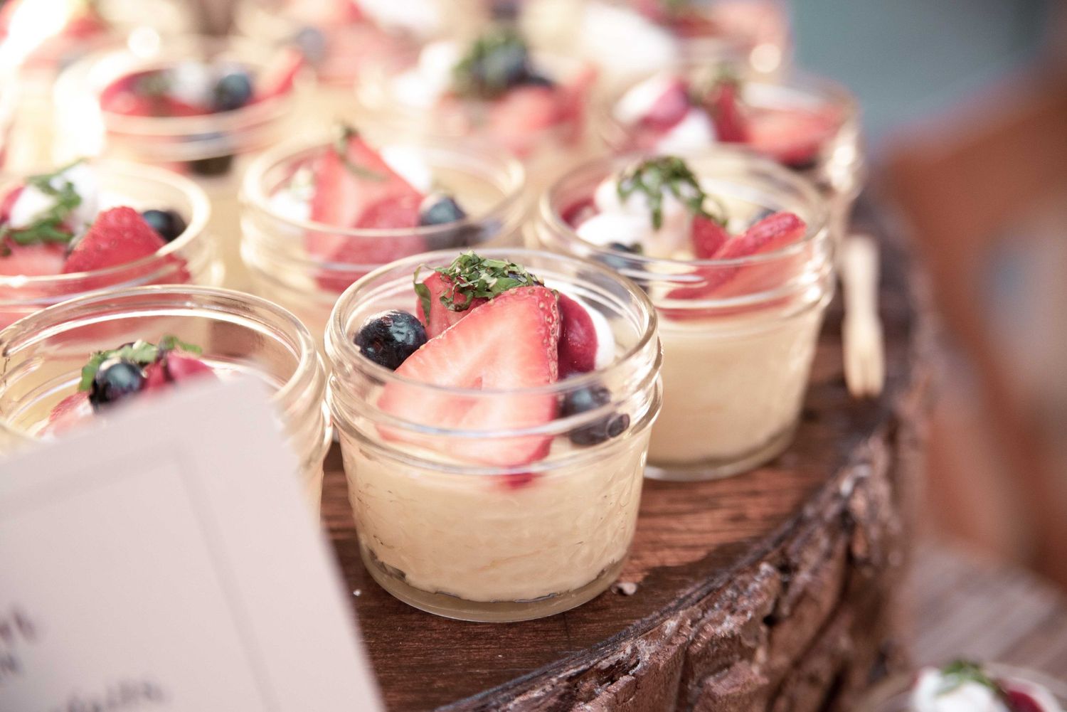 Mason jars filled with creamy dessert topped with fresh strawberries and blueberries displayed on a rustic wooden surface.