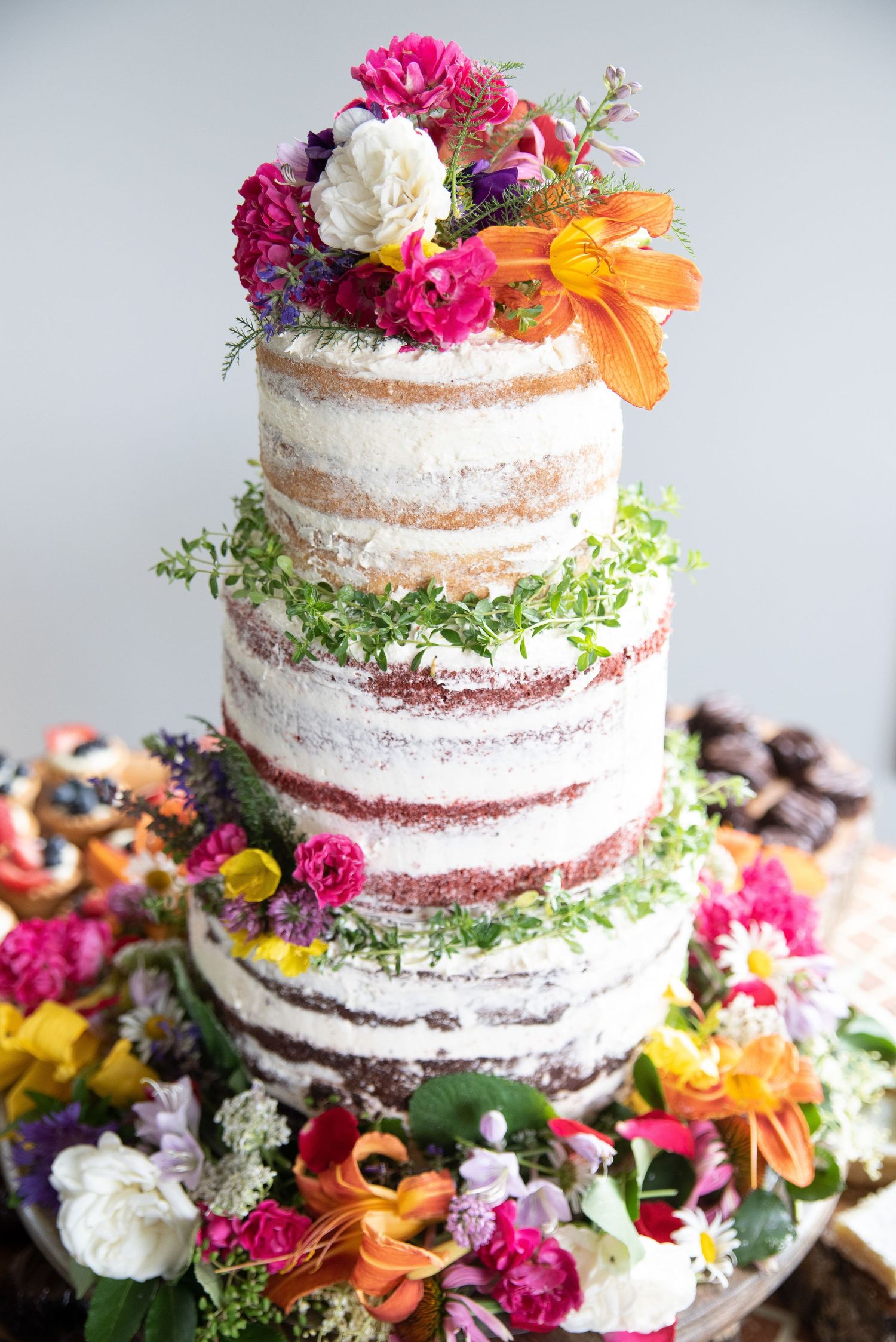 Three-tier naked wedding cake adorned with colorful fresh flowers.