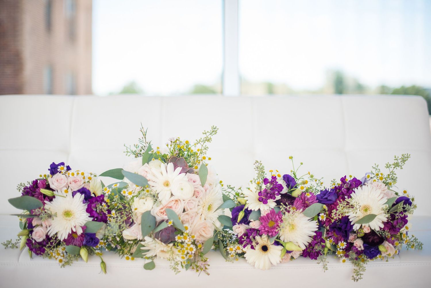 Colorful wedding bouquets with purple and white flowers arranged on a white reception table.