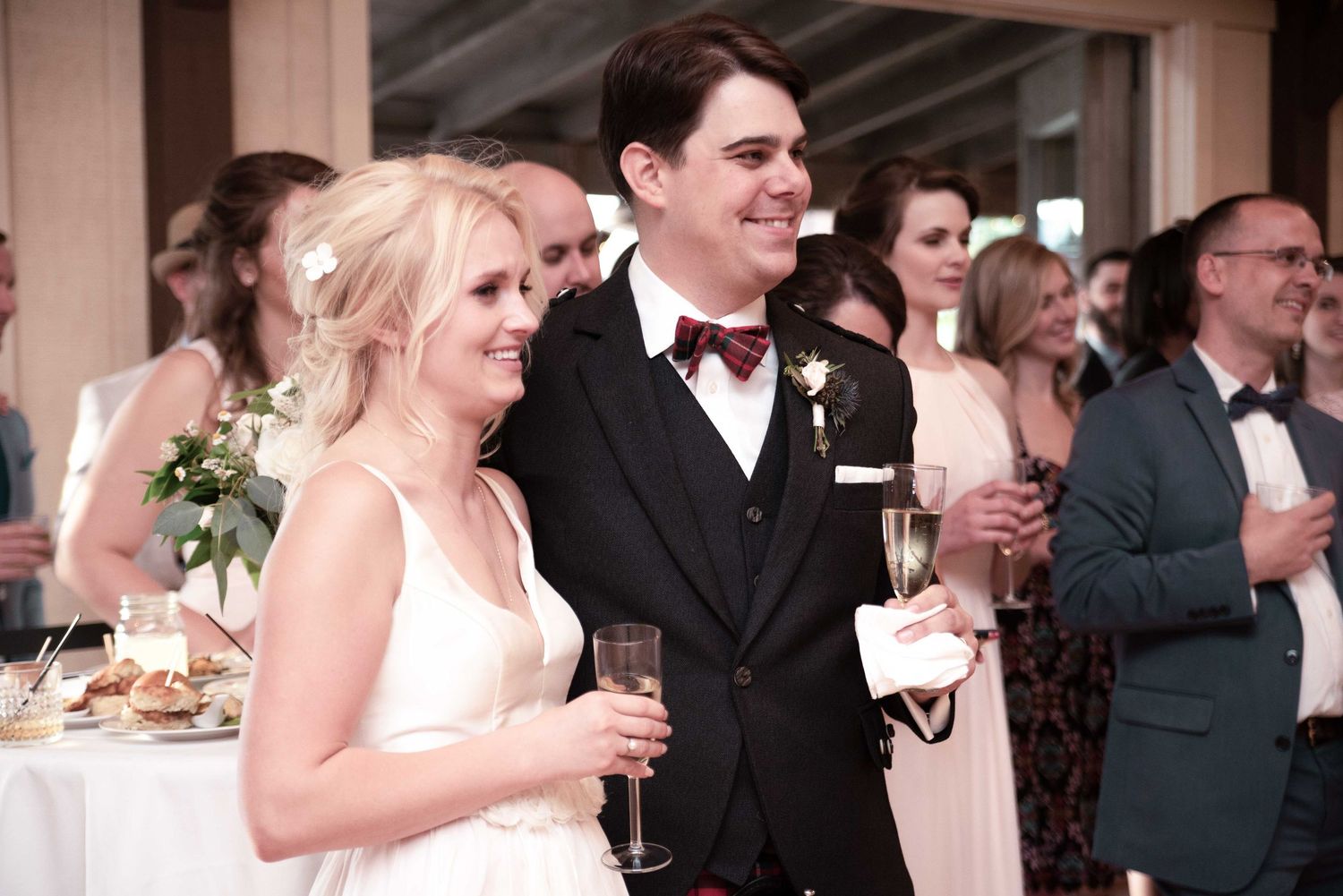 Bride and groom smiling and holding champagne glasses at their wedding reception celebration.