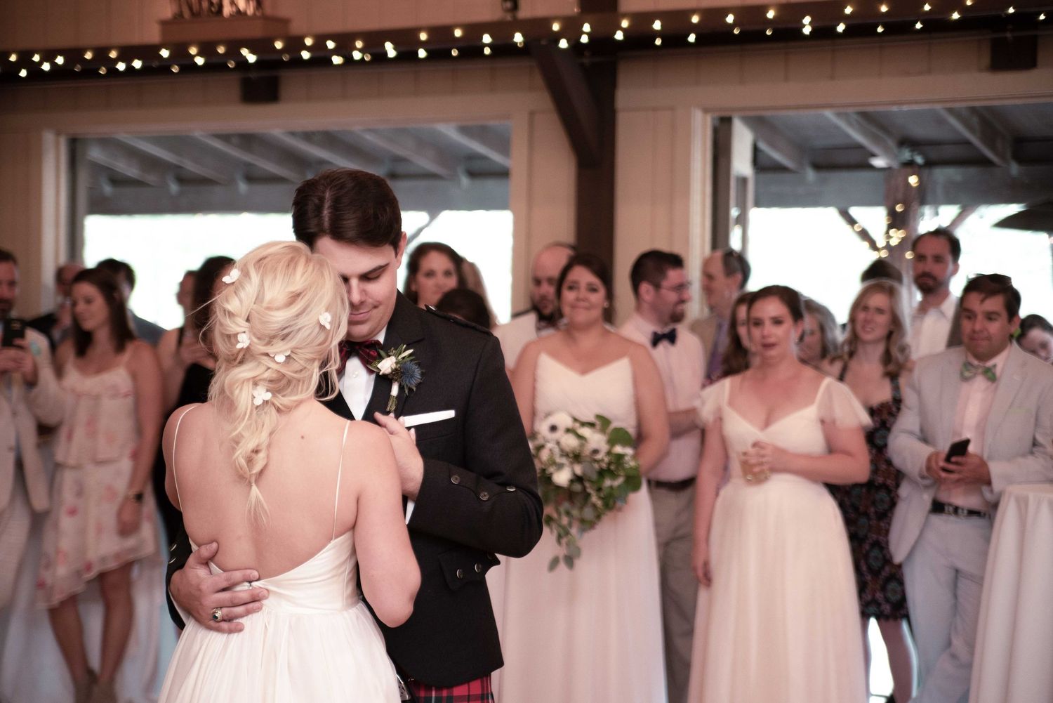Bride and groom share first dance at rustic barn wedding reception surrounded by bridesmaids and guests.