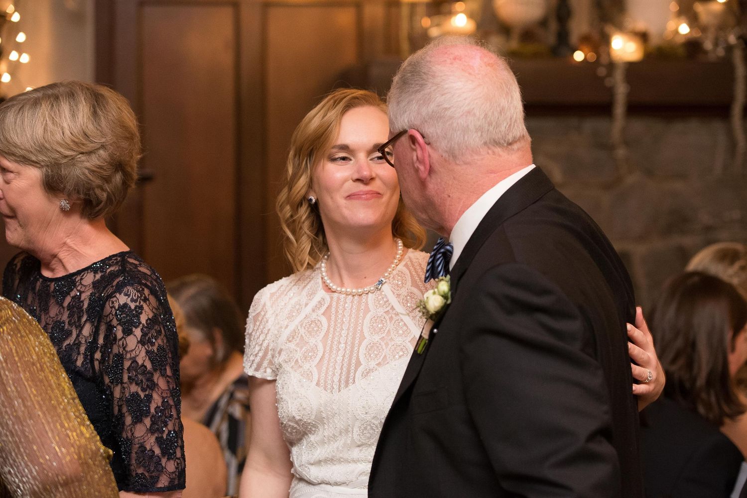 A woman in a white lace dress smiles while embracing a man in a suit at an elegant wedding reception.