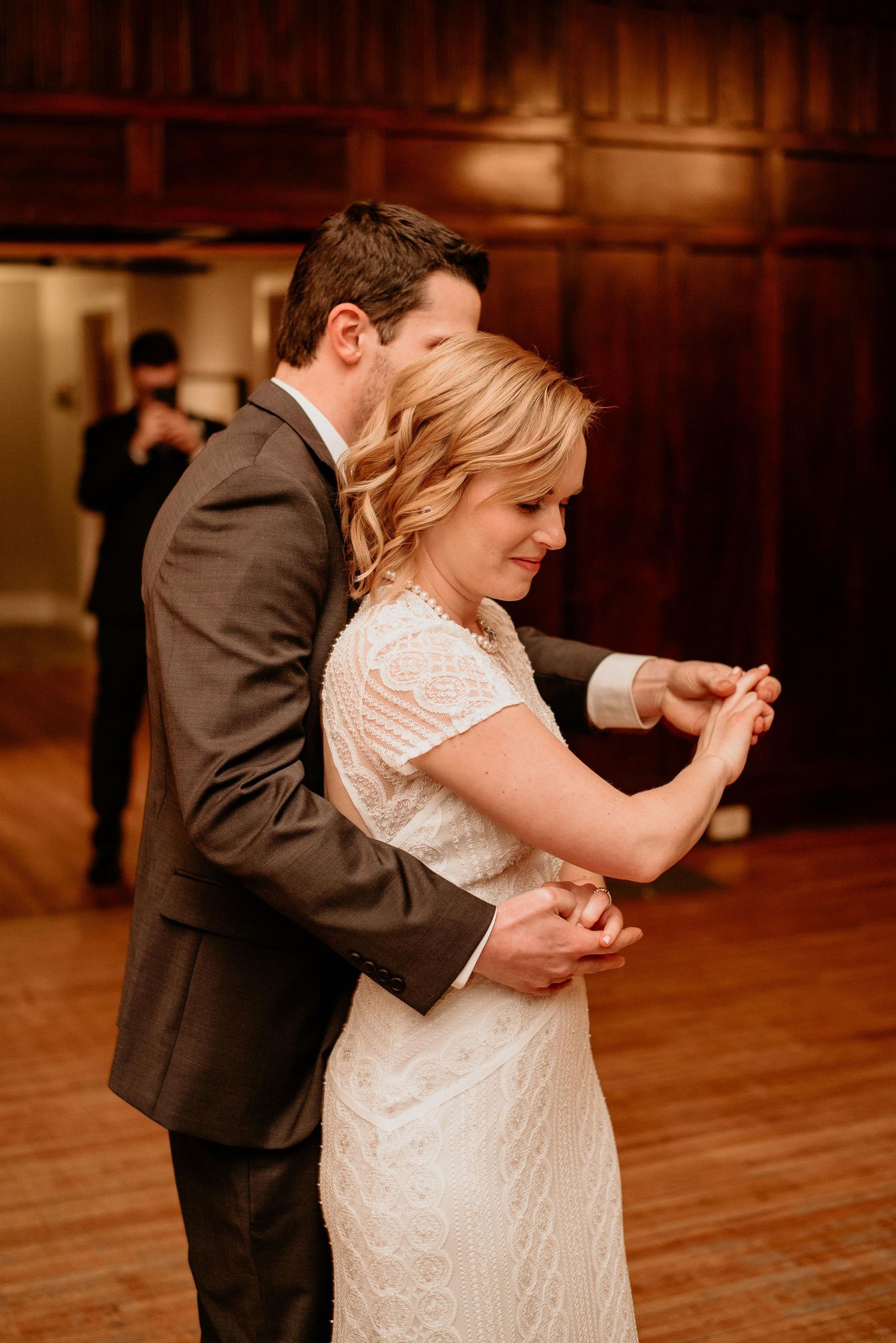Bride and groom share their first dance, with groom embracing bride in white lace dress at wedding reception.
