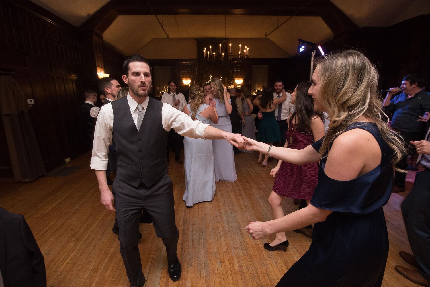 Couple dancing together at a wedding reception in an elegant wood-paneled ballroom with guests in background.
