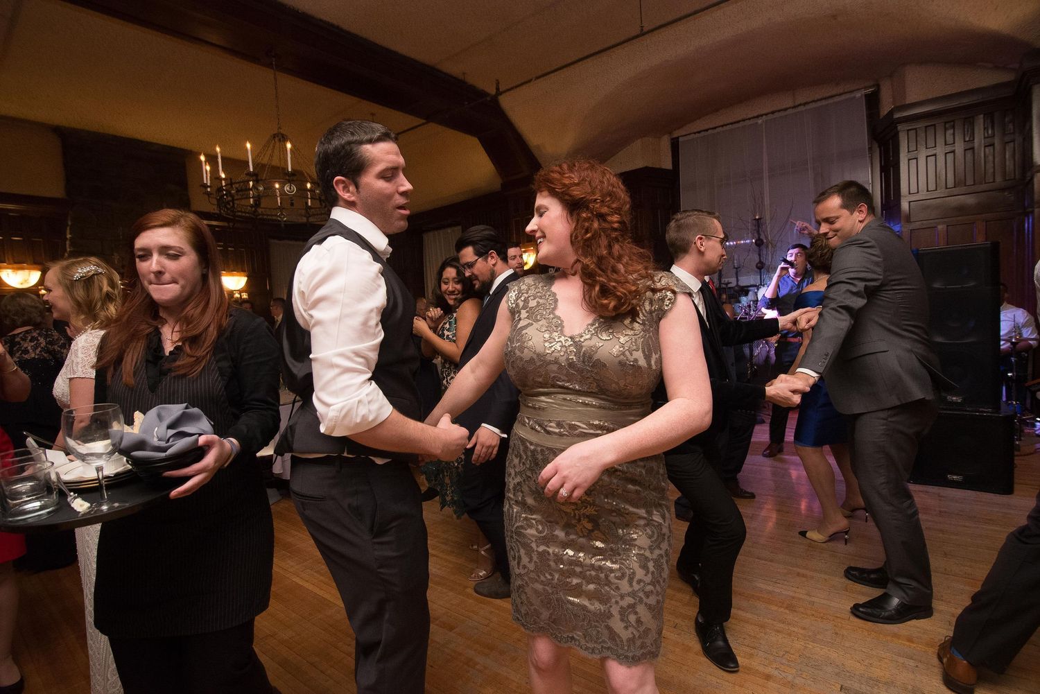 Guests dancing and socializing at an elegant indoor wedding reception in a warmly lit venue.