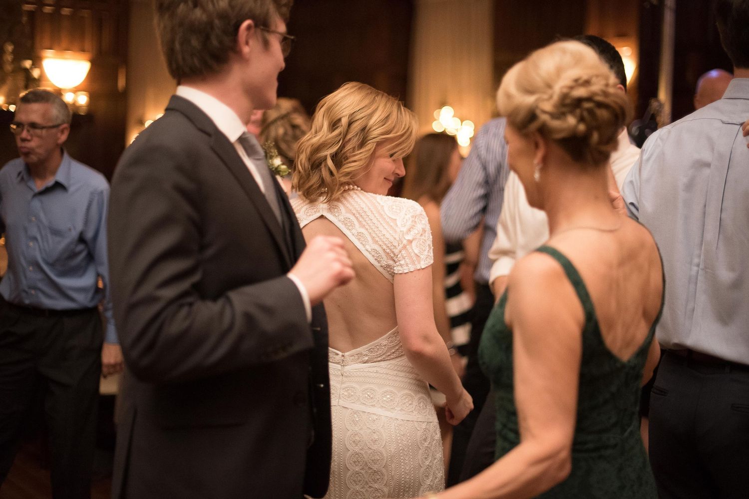 Bride in white lace backless gown dancing with guests at elegant wedding reception venue.