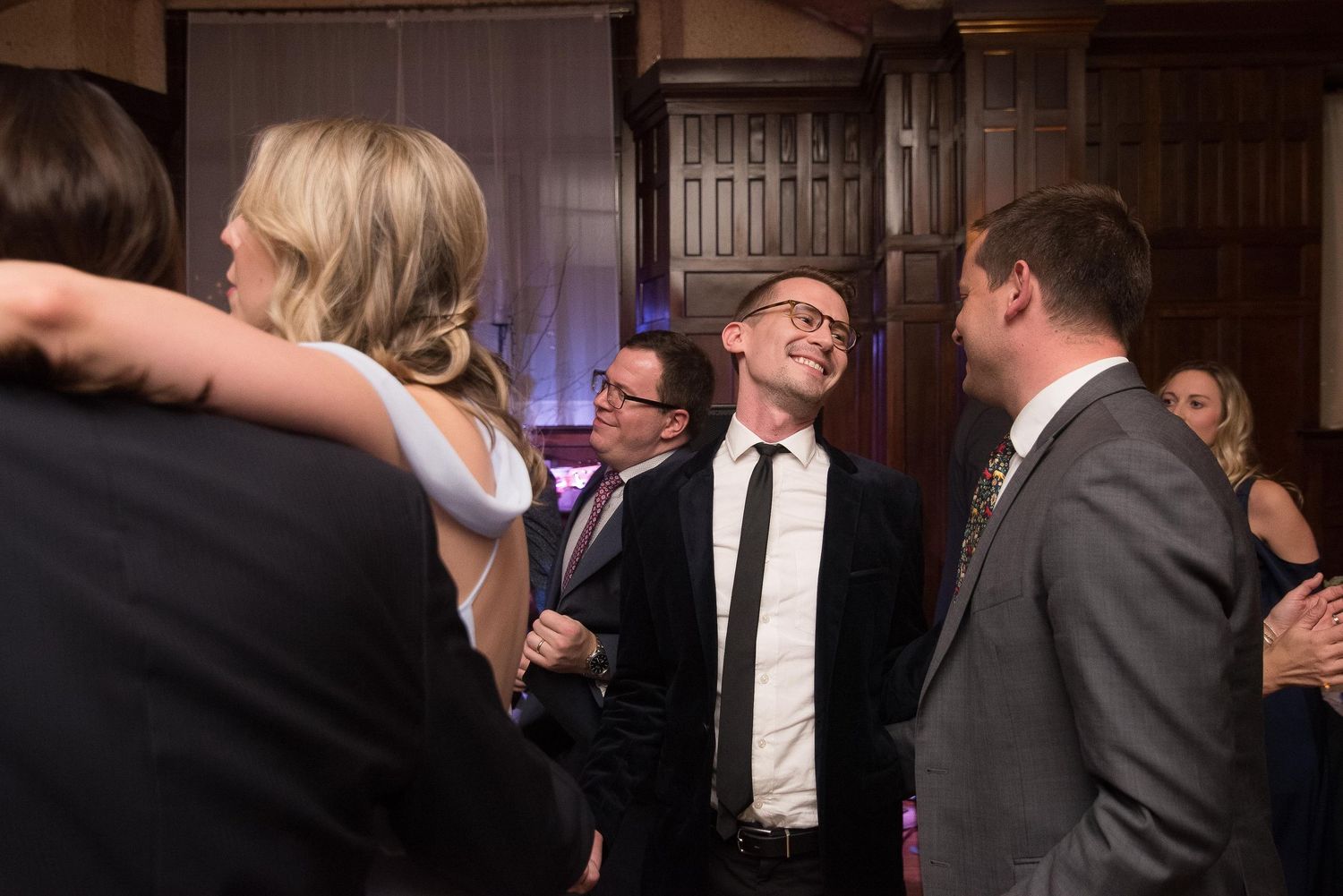 Guests mingling and laughing at an elegant indoor formal event in a wood-paneled venue.