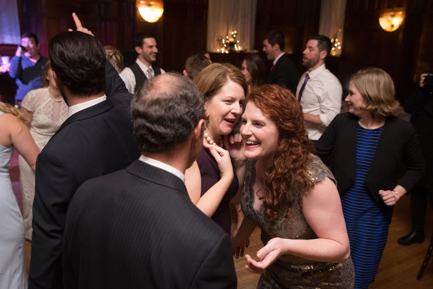 Guests laughing and dancing together at an elegant wedding reception in a grand ballroom.