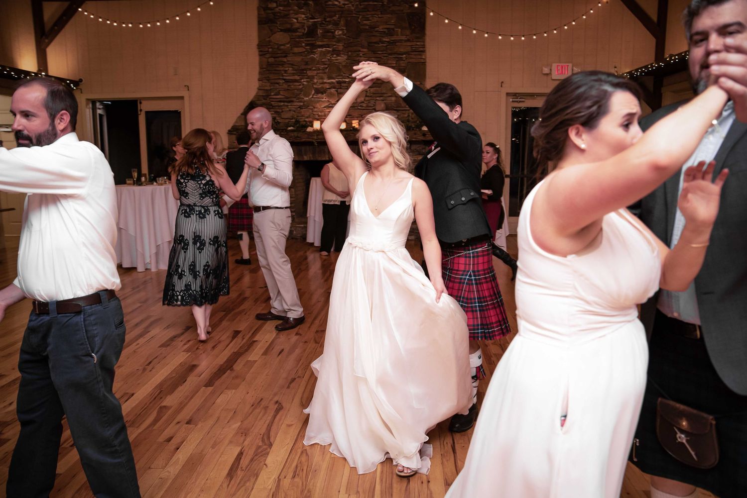 Bride in white gown twirls on dance floor at wedding reception with guests and bridesmaid dancing.