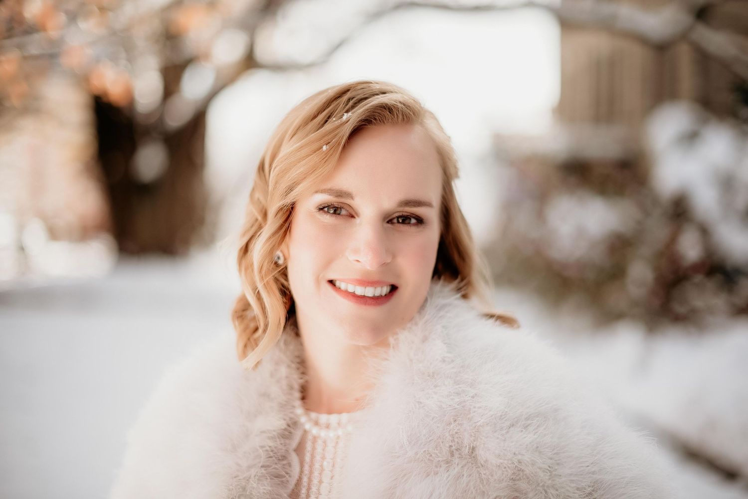 Smiling blonde woman in white fuzzy sweater posing outdoors in a snowy winter setting.