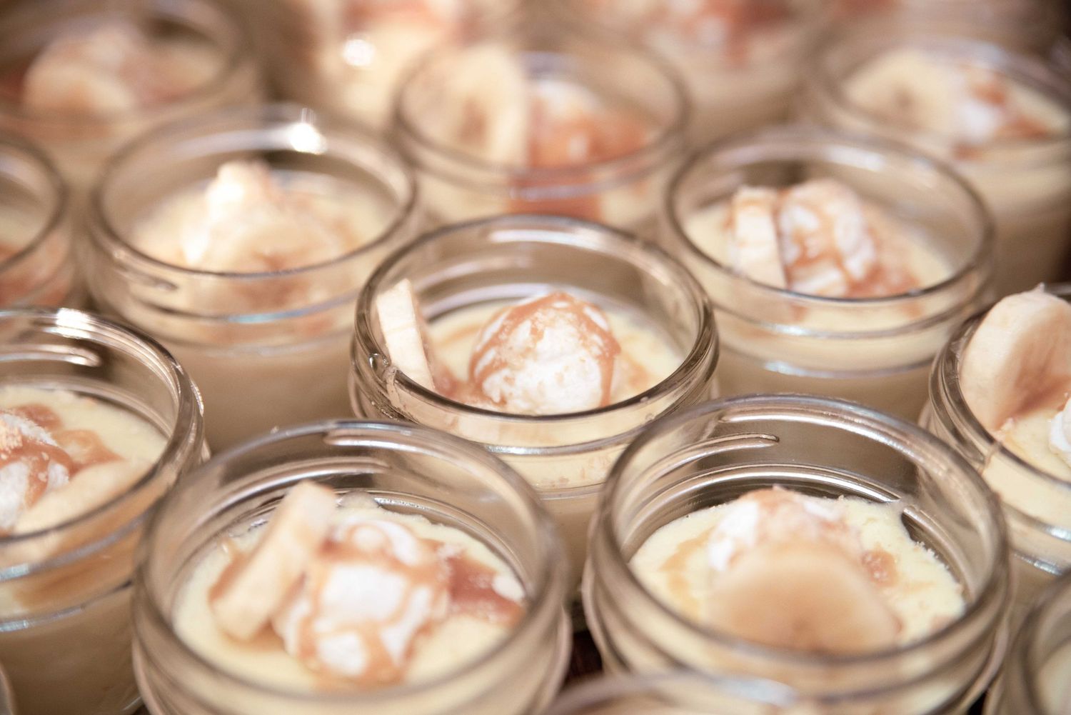 Close-up of creamy desserts in small glass jars with caramel swirls, arranged in rows for an elegant presentation.