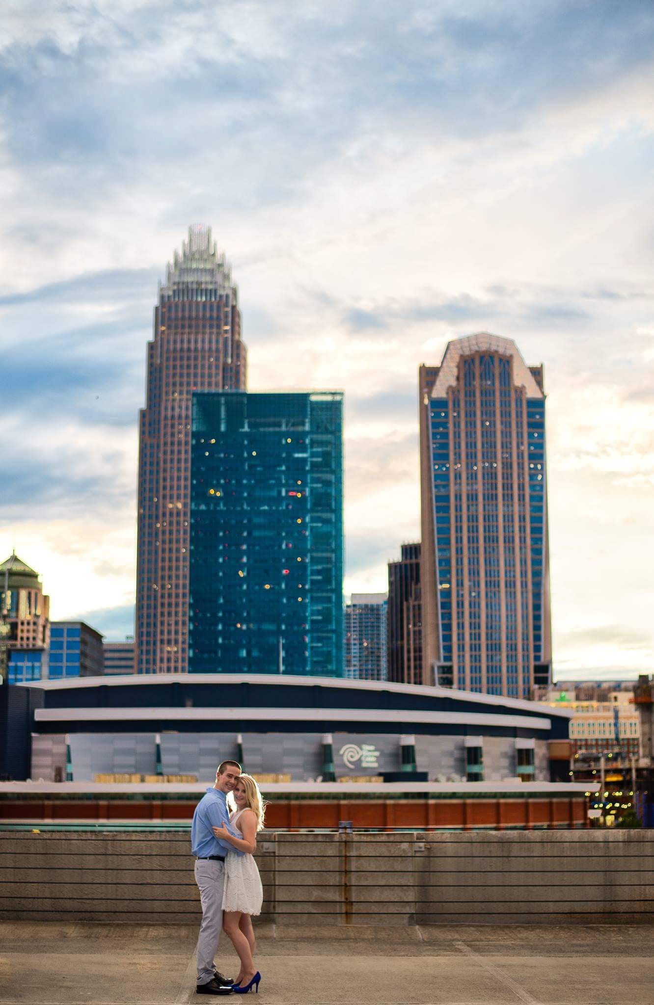 Couple sharing a romantic embrace on a rooftop with the Charlotte NC city skyline in the background at sunset.