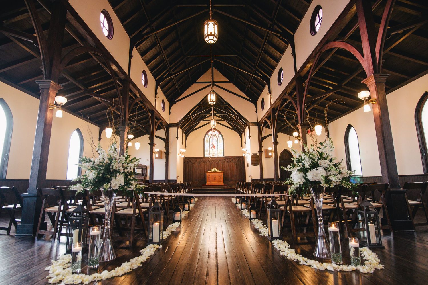 Elegant church wedding venue with wooden pews, floral arrangements, and rose petal aisle decor.