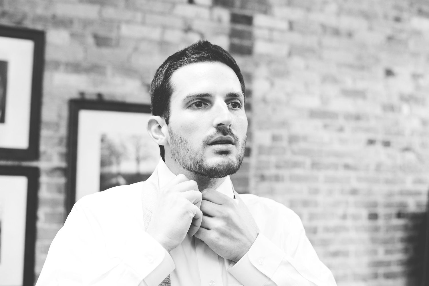 Man adjusting collar in black and white portrait photo against brick wall background.