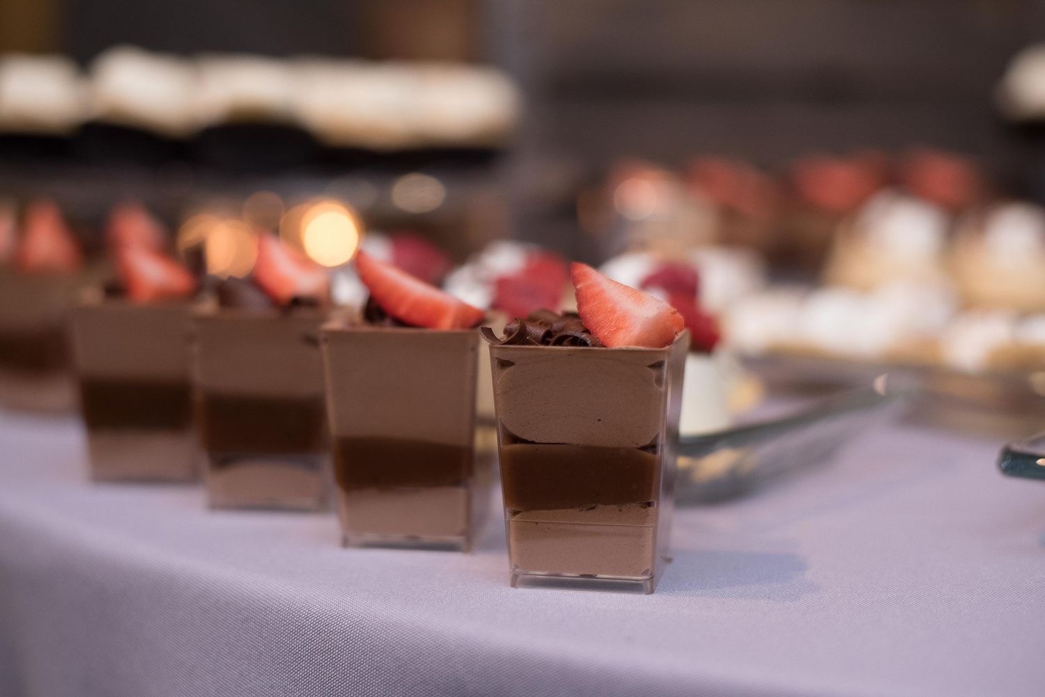 Elegant chocolate mousse dessert cups topped with fresh strawberries displayed on a table at a catered event.