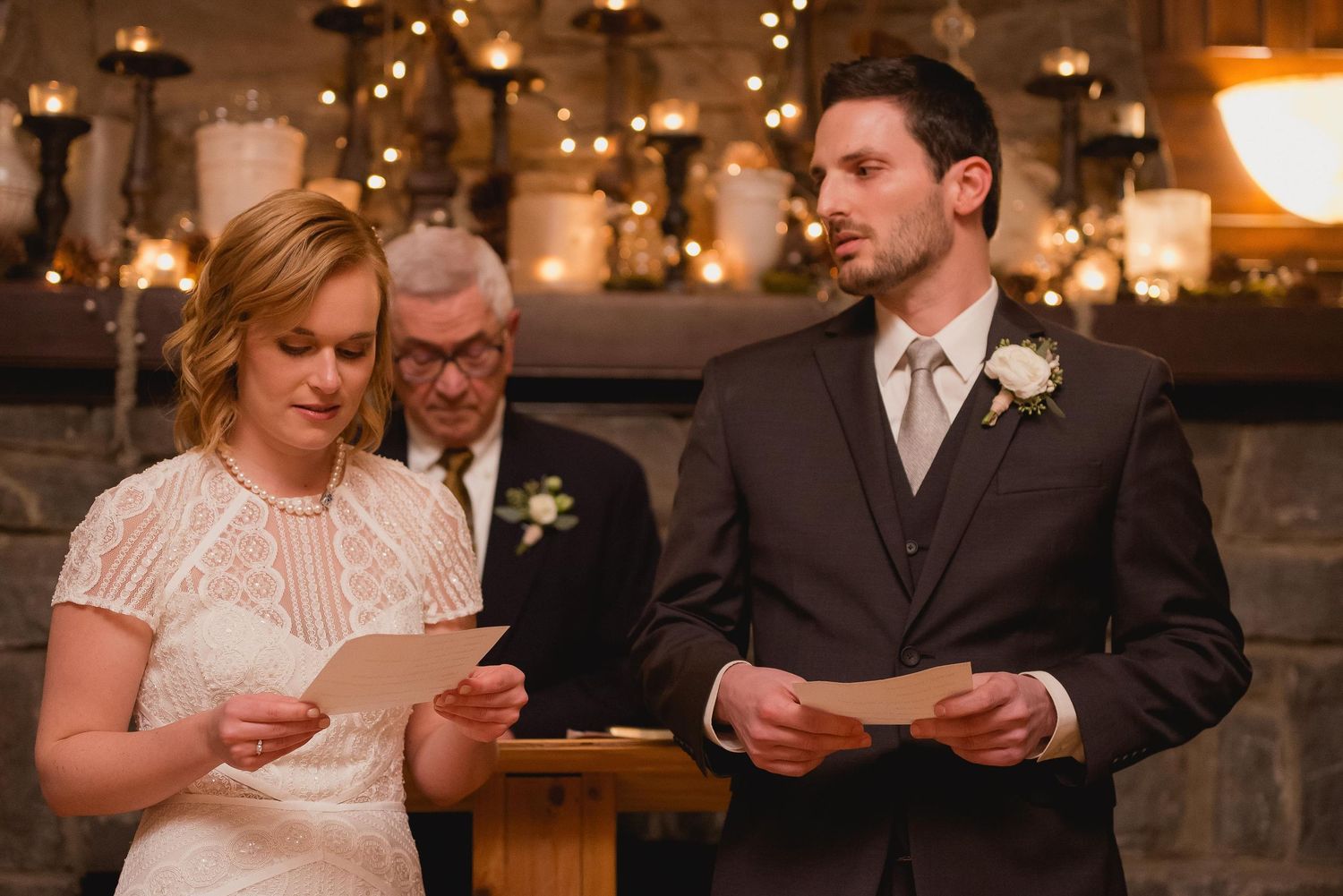 Bride and groom reading wedding vows at rustic candlelit ceremony with officiant standing behind them.