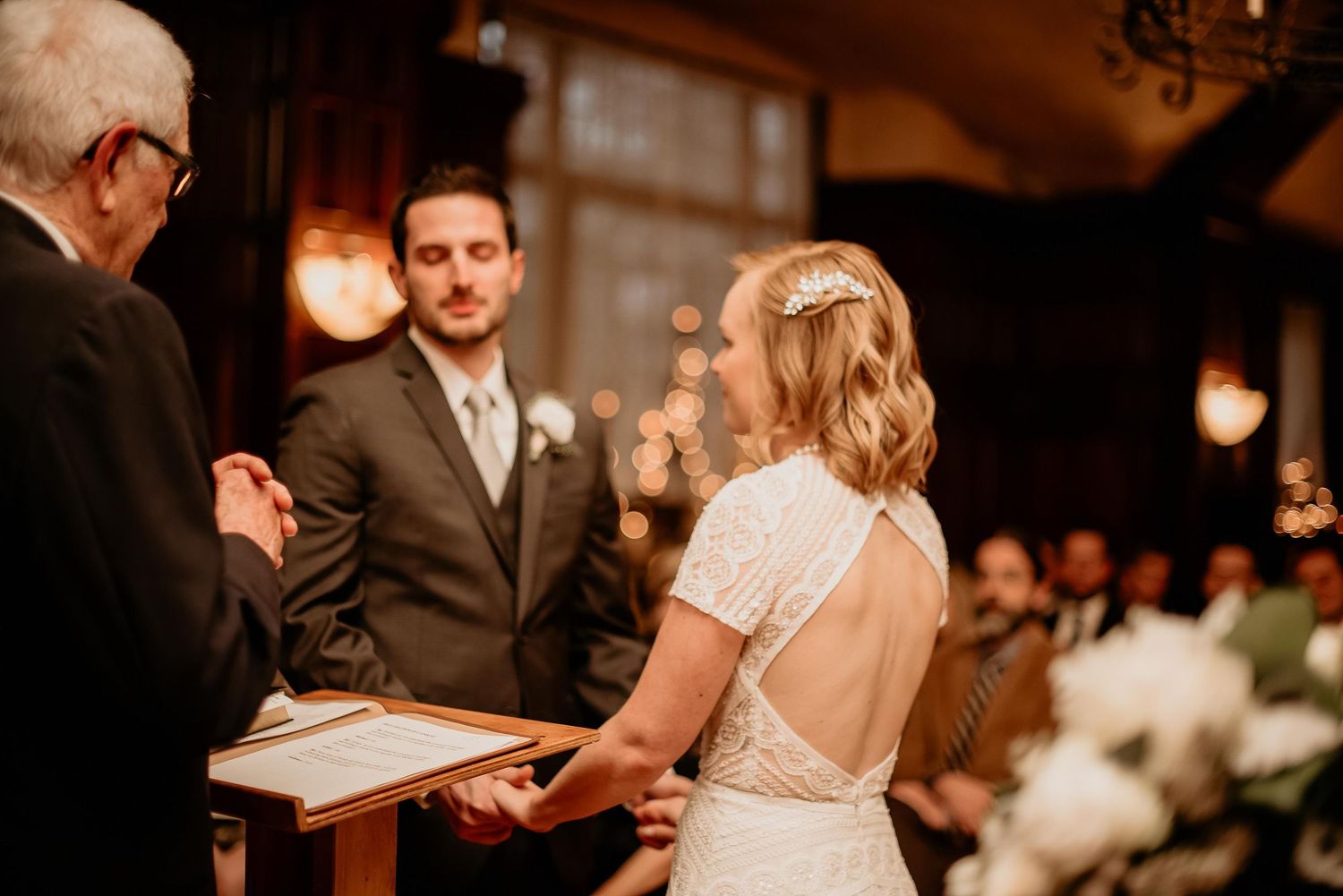 Bride and groom holding hands at altar during elegant indoor wedding ceremony with officiant.