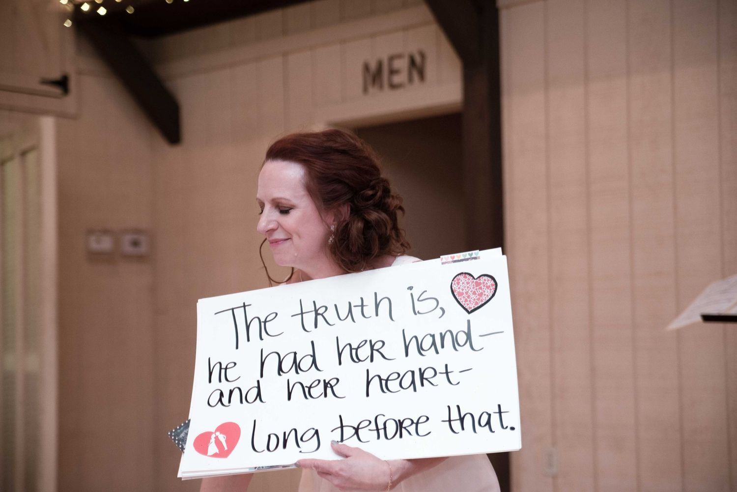 Woman holding a romantic handwritten sign reading 'The truth is, he had her hand and her heart long before that.'