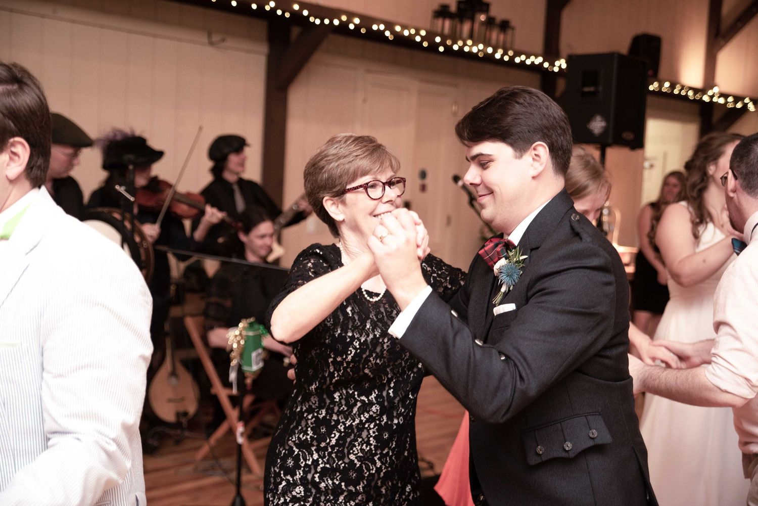 Couple dancing joyfully at a wedding reception with a live band performing in the background.
