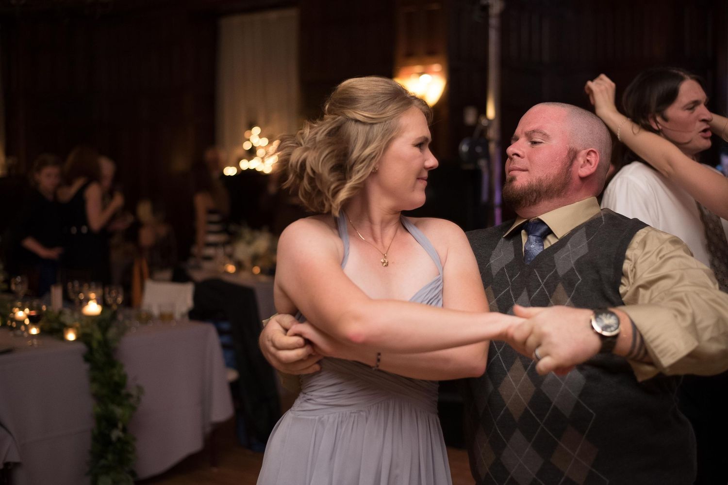 Couple sharing romantic dance at wedding reception, woman in gray bridesmaid dress dancing with man in argyle vest.