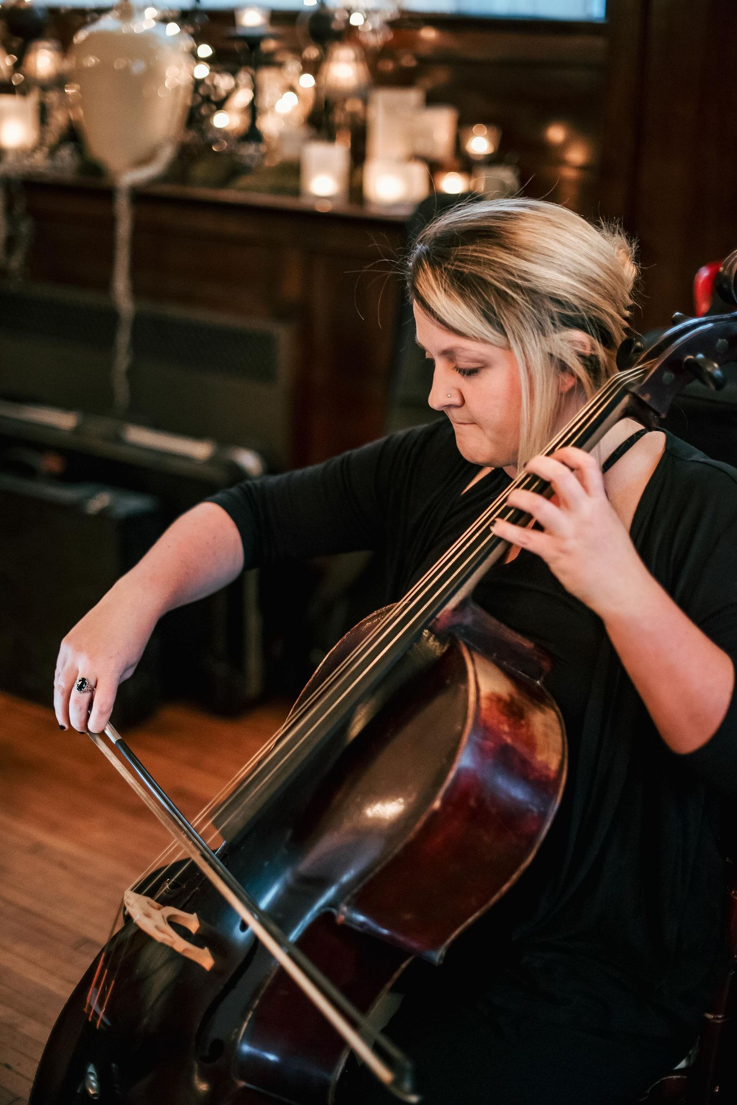 Woman in black dress playing cello at candlelit event, focused on performance with elegant updo hairstyle.